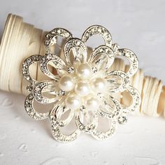 a white flower brooch sitting on top of a piece of cloth next to a spool of thread