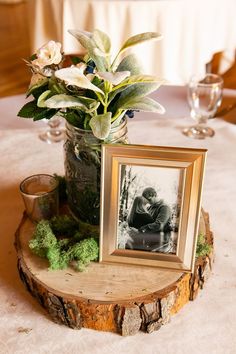 a vase with flowers and an old photo is on a tree stump at the table