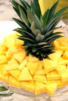 a pineapple sitting on top of a glass bowl filled with cut up pieces of fruit