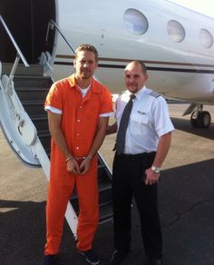 two men in orange jumpsuits standing next to an airplane