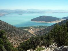 a scenic view of the lake and mountains from atop a hill with trees on it