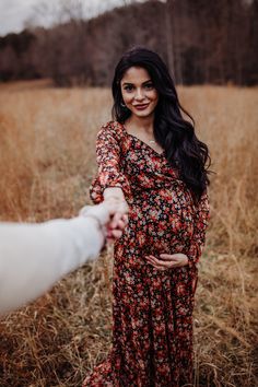 a pregnant woman holding her husband's hand in a field with tall brown grass