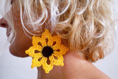 a woman with blonde hair wearing yellow crocheted flower earrings on her left ear