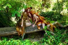 two beautiful women dressed as the little mermaids sitting on a log in the woods