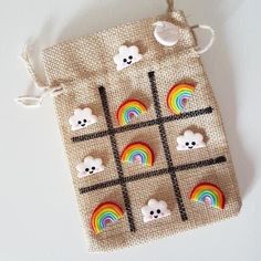 a cross stitch bag with rainbows, clouds and bears on the front is hanging from a string