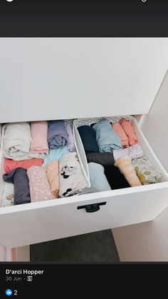 an open drawer filled with folded clothes on top of a white table next to a wall