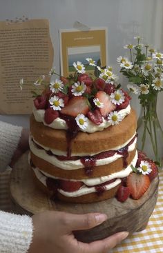 a cake with strawberries and daisies on top is being held by a person