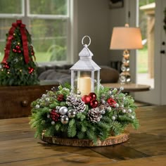 A holiday centerpiece of noble fir, white pine, incense cedar, silver glittery bead decorations, 2 red ball clusters, 2 silver ball clusters, 6 red berry clusters, 6 Australian pinecones with silver glitter, and an LED white lantern sitting on a wood round on a table up close. Christmas Lantern Centerpieces, Frosted Pinecones, Lantern Centerpiece, Christmas Decorations Centerpiece, Christmas Candle Decorations, Christmas Lantern