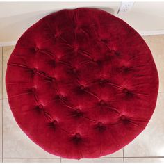 a red round ottoman sitting on top of a tile floor next to a white wall