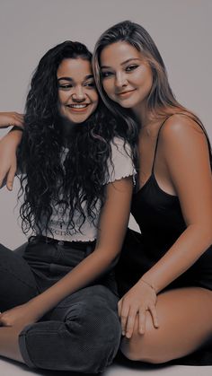 two young women sitting next to each other on top of a white floor with their arms around one another