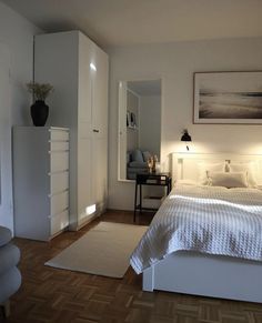 a white bed sitting next to a dresser and chair in a bedroom on top of a hard wood floor