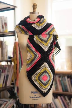 a crocheted scarf on a mannequin in front of bookshelves