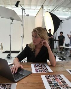 a woman sitting at a table with a laptop in front of her and people behind her