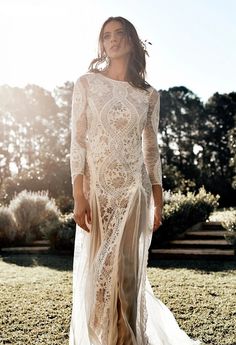 a woman is standing in the grass wearing a long white dress with sheer lace on it