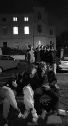 a group of people sitting on top of a park bench next to each other in front of a building