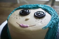 a cake decorated to look like a face with blue hair and buttons on it's head