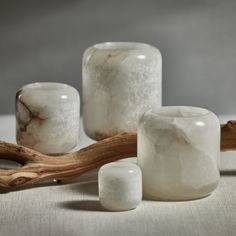 three white marble candle holders sitting next to each other on a table with driftwood