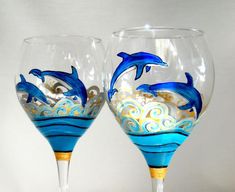 two hand painted wine glasses with dolphins on the bottom one is blue and gold, while the other is white