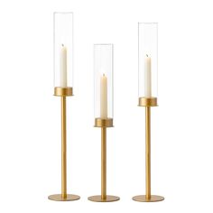 three brass candles with clear glass cylinders on each candle holder, one is lit and the other is turned off