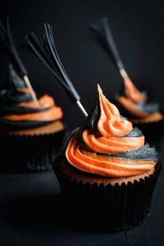 three cupcakes with orange frosting and black sticks sticking out of the top