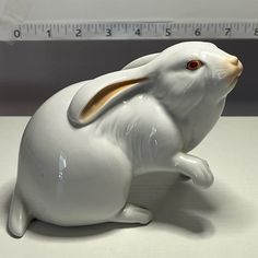 a white rabbit figurine sitting on top of a table next to a ruler