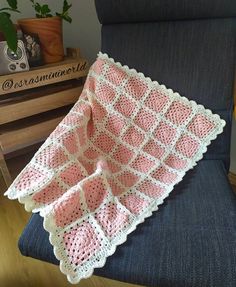 a pink and white crocheted blanket sitting on top of a chair next to a potted plant