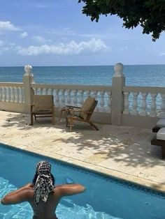 a woman standing in the pool looking out at the ocean