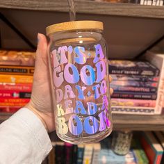 a person holding a glass jar with writing on it in front of bookshelves