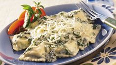 a blue plate topped with ravioli covered in cheese and spinach next to a fork