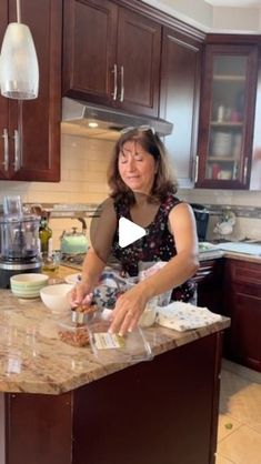 a woman in a kitchen preparing food on top of a marble countertop next to wooden cabinets