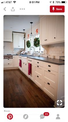 a kitchen with white cabinets and black counter tops is decorated for the holiday season by wreaths hanging on the windows