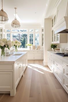 a large kitchen with white cabinets and wooden floors is pictured in this image, there are two chandeliers hanging from the ceiling