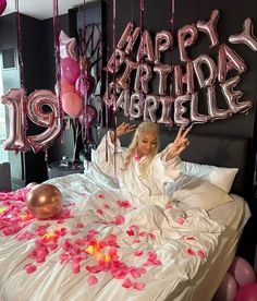 a woman laying on top of a bed surrounded by balloons and streamers in the shape of letters