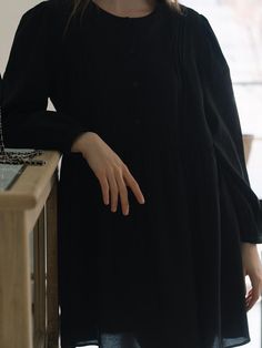 This dress exhibits a relaxed fit with a gathered waistline, creating a flared skirt that enhances its loose silhouette. It features a round neckline and a button-up front, which continues halfway down, providing a balance between structure and ease. The long sleeves are finished with elastic cuffs, adding a slight volume to the arms. The fabric looks soft and possibly lightweight, which contributes to the flowy nature of the dress.- The gathered waistline not only accentuates the dress's shape but also allows for comfortable wear.- With its simple and versatile design, this dress could be accessorized in multiple ways to suit different occasions.- The dress's button-up detail adds a classic touch, while the dark tone gives it an air of sophistication. Casual Long-sleeved Midi Dress With Gathered Waist, Casual Long Sleeve Midi Dress With Gathered Waist, Workwear Long Sleeve Midi Dress With Gathered Waist, Long Sleeve Midi Dress With Gathered Waist For Work, Casual Dresses With Pleated Billowy Sleeves, Black Workwear Dresses With Gathered Sleeves, Black Long Sleeve Dress With Pleated Hem, Black Midi Dress With Gathered Waist For Work, Black Dress With Pleated Sleeves For Daywear