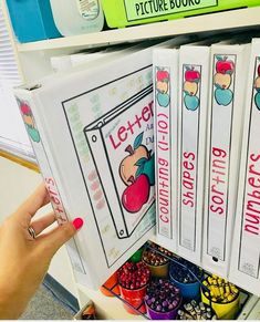 a hand is pointing at several books in a bookcase that are filled with pictures