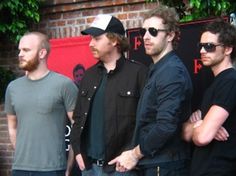 three men standing next to each other in front of a brick wall