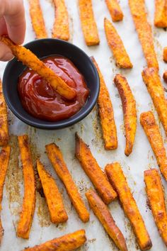 a person dipping something into a black bowl filled with sweet potato fries on top of a table