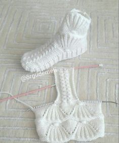 two white knitted socks are laying on the floor next to each other with yarn in them