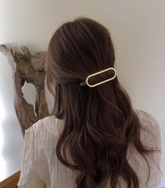 the back of a woman's head wearing a gold hair clip with wavy brown hair