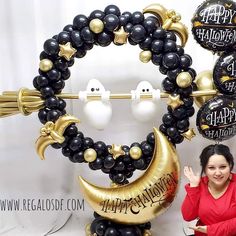 a woman standing in front of balloons that say happy halloween and crescent moon with faces on them