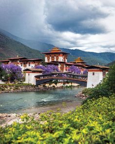 a bridge over a river in front of a large building with flowers on the side