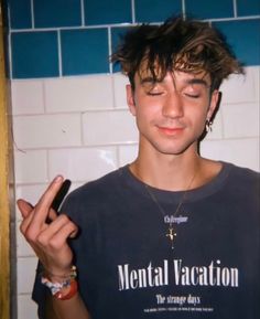 a young man with his eyes closed holding a cell phone in one hand and making the peace sign