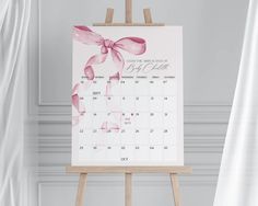 an easel with a calendar on it in front of a white wall and curtains