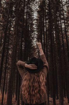 a woman standing in the middle of a forest with her hands up to her head