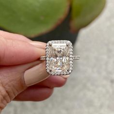 a person holding an engagement ring with a large diamond in the center and surrounded by smaller diamonds