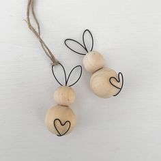 two wooden beads with black hearts on them hanging from twine strings against a white background