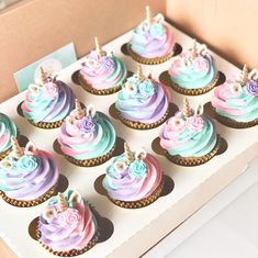 cupcakes with pastel frosting and unicorn decorations in a box