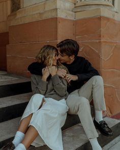 a man and woman are sitting on the steps with their arms around each other as they kiss