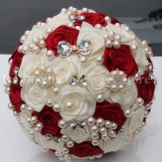 a bridal bouquet with red roses and pearls on the bottom is sitting on a table