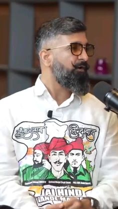 a man with a beard and glasses sitting in front of a microphone while wearing a t - shirt